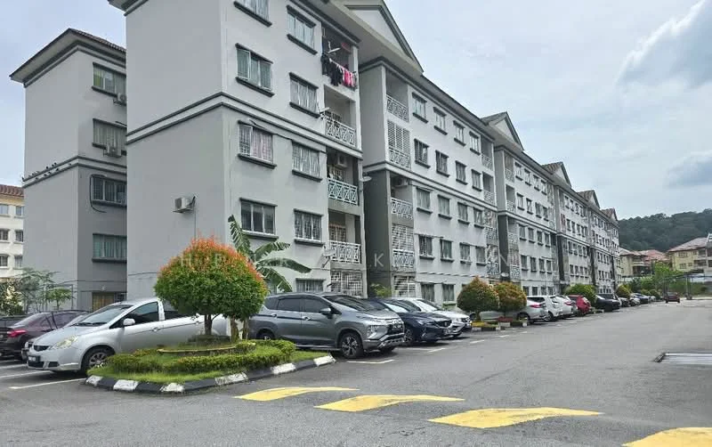 Exterior type: low-rise apartment block; features: grey painted facade, 3-storey building, balconies with decorative railings, landscaped garden with shrubs, open-air parking lot, driveway with painted lines, surrounded by greenery, multiple parked cars; style: modern.