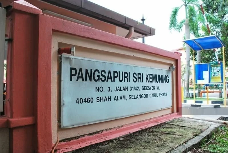 Exterior type: low-rise apartment block; features: signage with building name, pink painted facade, landscaped area, surrounding greenery, paved walkway, street view; style: modern.