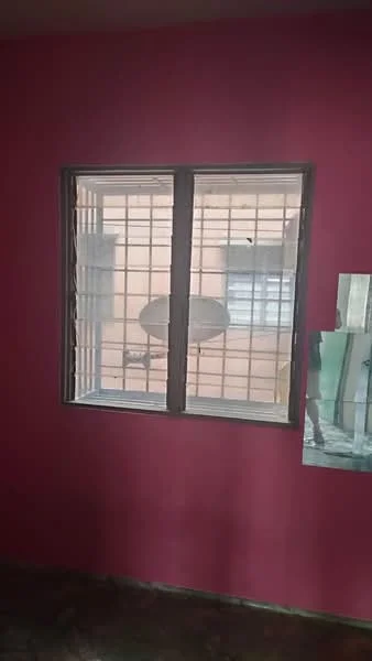 Room features: pink painted walls, window with metal grille, visible outdoor view, flooring with tiles, corner of a mirror, light source from window.