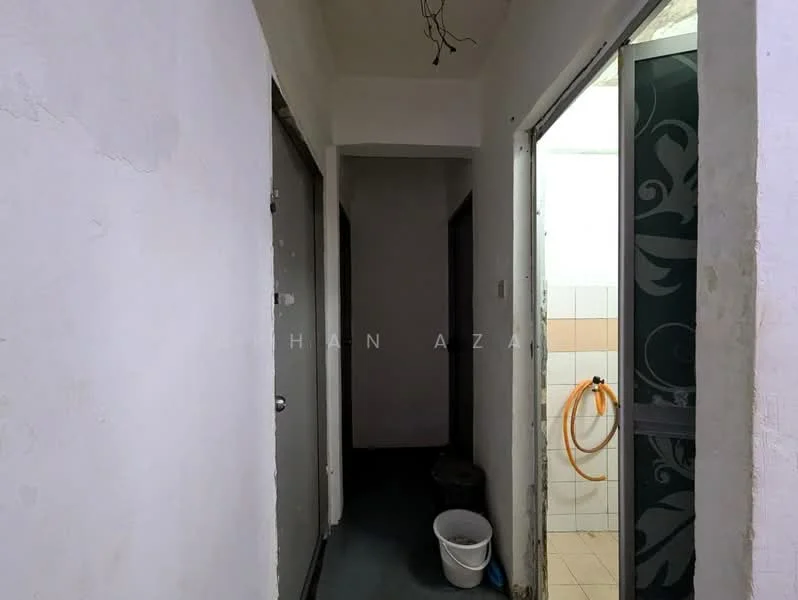 Room features: white painted walls, dark flooring, door frames, light fixture hanging from ceiling, bucket, visible plumbing hose, tiled wall, door to bathroom, narrow hallway.