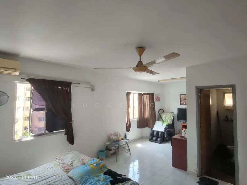 Room features: white painted walls, ceiling fan, wall-mounted split AC, tile flooring, two windows with dark curtains, bed with bedding, small side table, wooden cabinet, black leather recliner chair, decorative plants, TV on a stand.