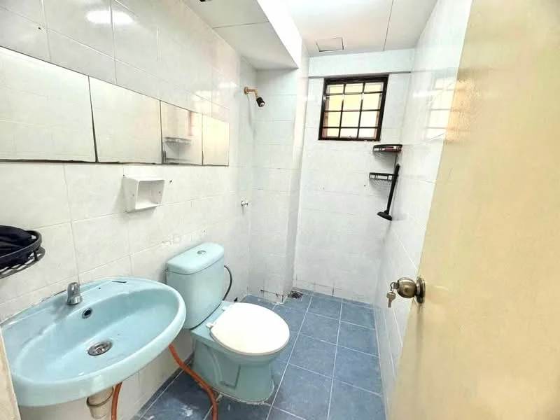 Bathroom features: white tiled walls, blue ceramic tile flooring, single-sink vanity with chrome faucet, one-piece toilet, framed mirror above sink, window with metal grille, wall-mounted shelf, exposed plumbing, light fixture on ceiling.