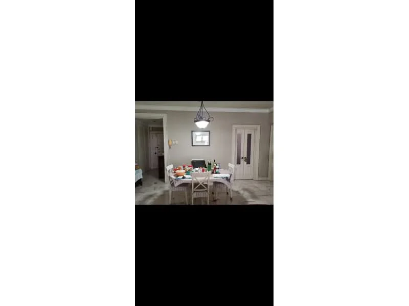 Dining features: dining table with white surface, 4 white wooden chairs, chandelier light fixture, grey painted walls, marble tile flooring, decorative wall art, glass door, bottles and dishes on the table; style: modern.