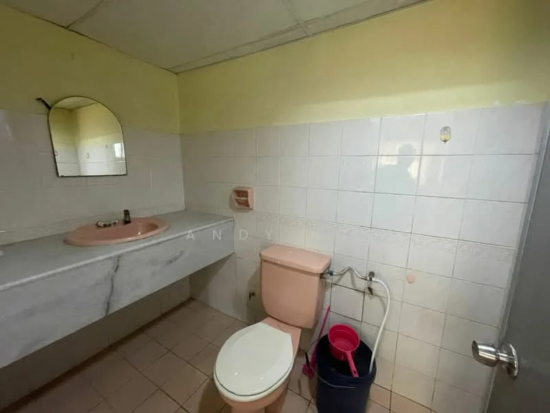 Bathroom features: pink marble countertop, single-sink vanity, framed mirror, white tiled walls, light yellow painted walls, one-piece toilet, pink toilet tank, ceramic tile flooring, toilet brush, bucket, wall-mounted soap dispenser.