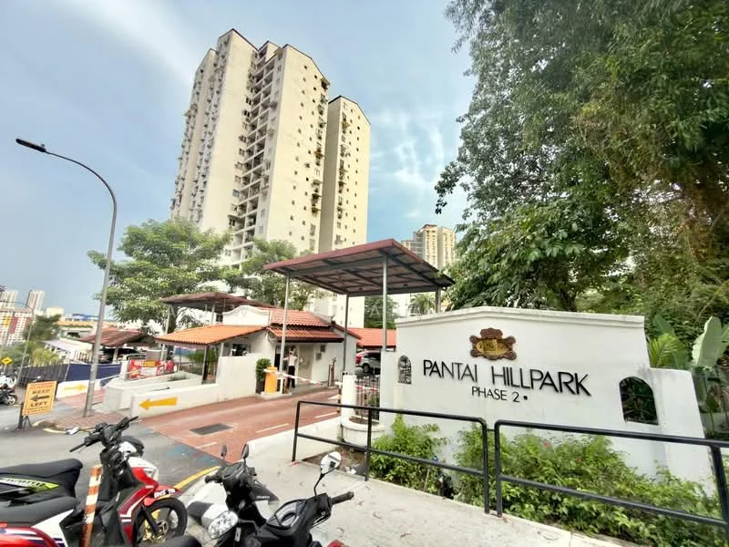Exterior type: high-rise condominium; features: white painted facade, red tiled roof, guard house at entrance, gated entry, landscaped greenery, parking area with motorcycles, signage for Pantai Hillpark Phase 2, surrounded by urban context; style: modern.