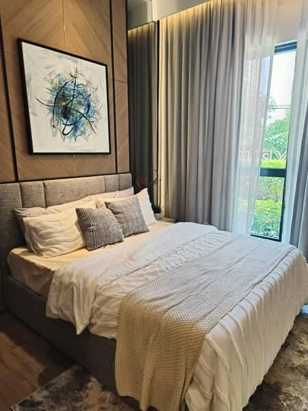Bedroom features: king-size bed with grey upholstered headboard, white bedding with decorative pillows, wooden flooring, large window with sheer curtains, framed artwork on wall, accent wall with wood paneling, bedside table, decorative plant on window sill, area rug with geometric pattern, recessed lighting; style: modern; view: garden.