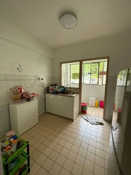 Kitchen features: white painted walls, cream tiled flooring, single-bowl stainless-steel sink, chrome pull-down faucet, white cabinetry, countertop with space for appliances, window with view to outside, refrigerator, storage cart with multiple shelves, various food items on countertop, cleaning supplies visible, open layout to adjacent area; view: garden.
