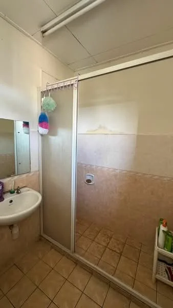 Bathroom features: single-sink basin, mirror above sink, glass shower enclosure, tile flooring, beige wall tiles, shower head, toilet, shelf with toiletries.
