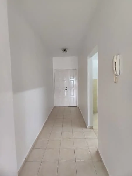 Hallway features: white painted walls, tile flooring, ceiling light fixture, intercom system, door at end of hallway, doorway to adjacent room.