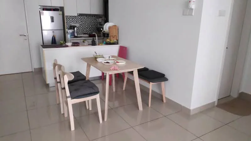 Dining features: light wood dining table, 4 dining chairs with grey cushions, ceramic plates on the table, white walls, grey tiled flooring, kitchen area visible in background, stainless-steel fridge, black and white patterned backsplash, open kitchen layout; style: modern.
