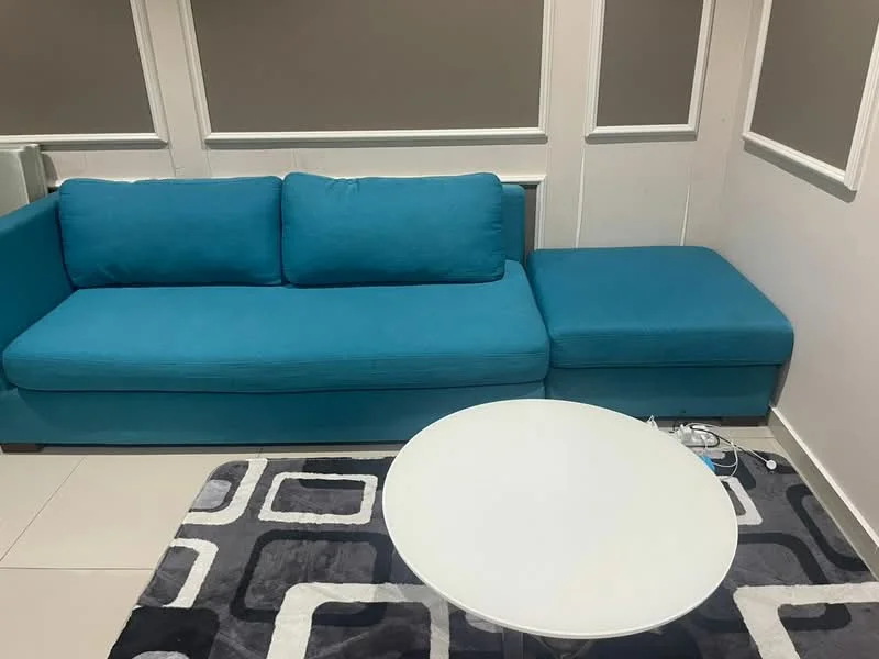 Living features: L-shape sectional sofa in turquoise, white round coffee table, area rug with geometric pattern in grey and black, cream painted walls, grey accent wall, tile flooring, wall-mounted electrical outlets; style: modern.