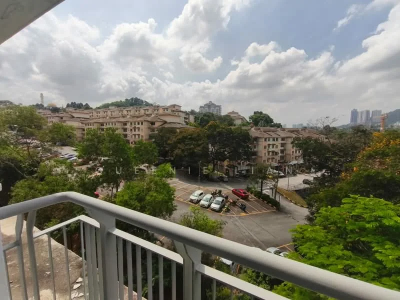 Exterior type: low-rise apartment block; features: view of surrounding buildings, landscaped greenery, open parking area, tree-lined streets, cloudy sky, balcony railing, multiple vehicles visible, hills in background; style: modern.