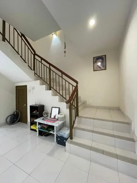Room features: white painted walls, tile flooring, staircase with wooden railing, wall-mounted light fixture, framed artwork on wall, small table with decorative items, door leading to another room, fan on the floor; style: modern.