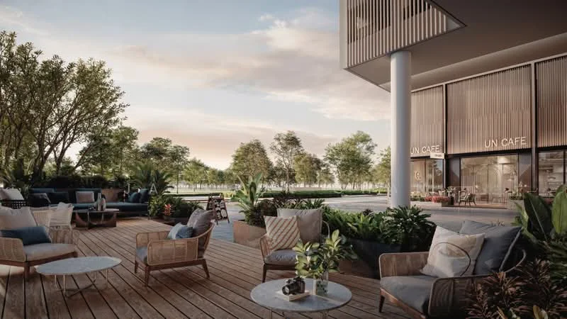 Exterior type: clubhouse; features: outdoor seating area, wooden deck flooring, landscaped garden with trees, planters with greenery, glass facade of cafe, outdoor lounge chairs, small round coffee tables, canopy shade structure, decorative cushions, modern outdoor furniture; style: modern.