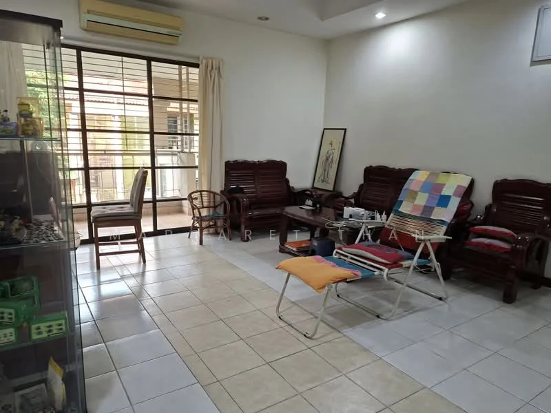 Living features: white painted walls, tile flooring, large windows with metal grills, ceiling-mounted air conditioning unit, wooden armchairs, folding lounge chairs, colorful throw blanket, framed artwork, glass display cabinet, natural light from windows.