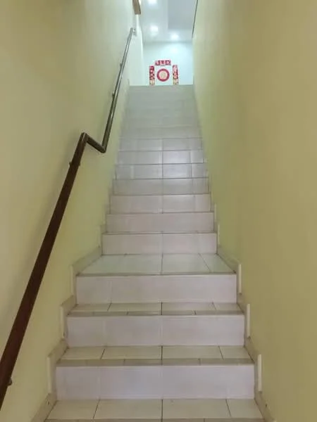 Room features: white tiled flooring, yellow painted walls, handrail on the right side, staircase with even steps, bright lighting at the top of the stairs.