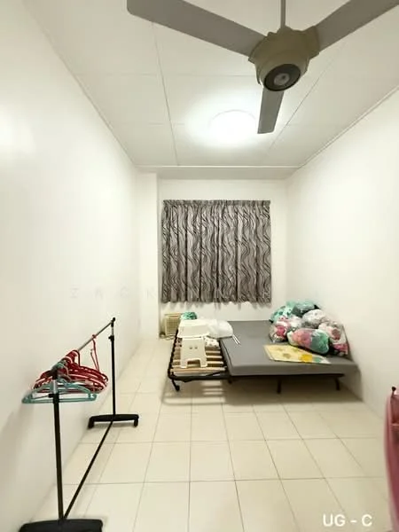 Room features: white painted walls, tile flooring, ceiling fan, window with patterned curtains, single bed frame, mattress, clothes rack, plastic storage boxes, stool.
