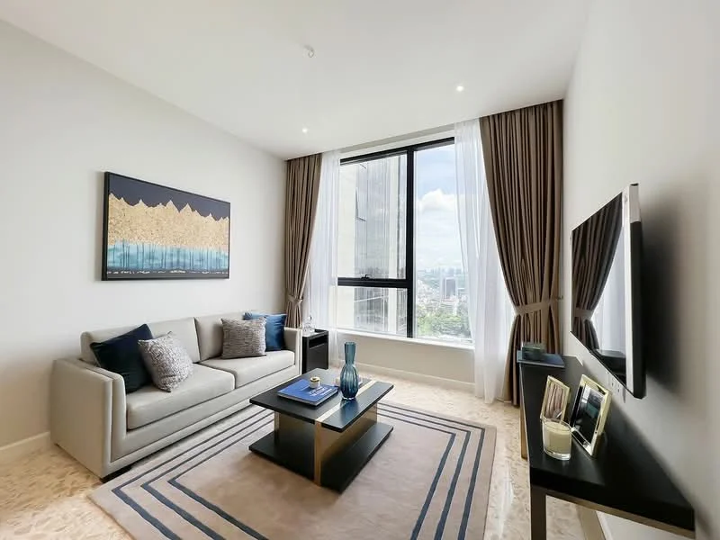 Living features: 3-seater fabric sofa in light grey, decorative cushions in navy blue, coffee table with black top and gold legs, area rug with geometric pattern, wall-mounted TV, framed artwork with abstract design, floor-to-ceiling windows, sheer curtains, light-colored walls, recessed downlights; style: modern; view: city.