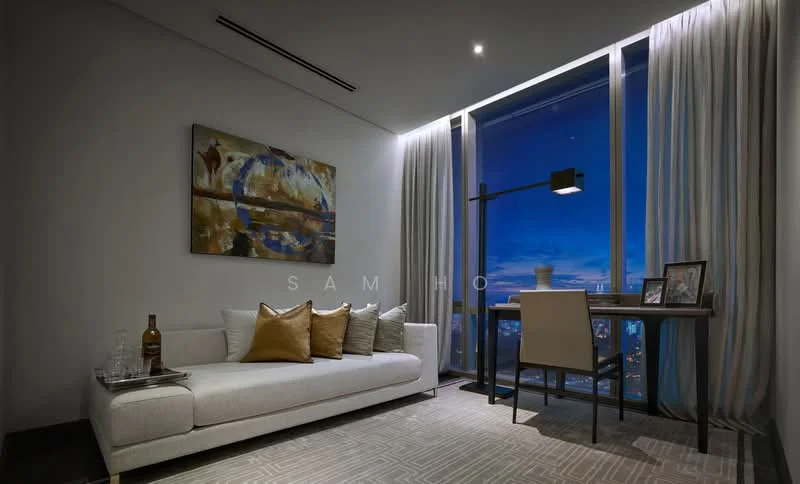 Living features: white fabric sofa, decorative cushions in gold and grey, abstract artwork on wall, wooden side table, desk with lamp, floor-to-ceiling windows, sheer curtains, recessed downlights, area rug with geometric pattern, glass vase on desk, bottle on side table, framed photos on desk; style: modern; view: city.