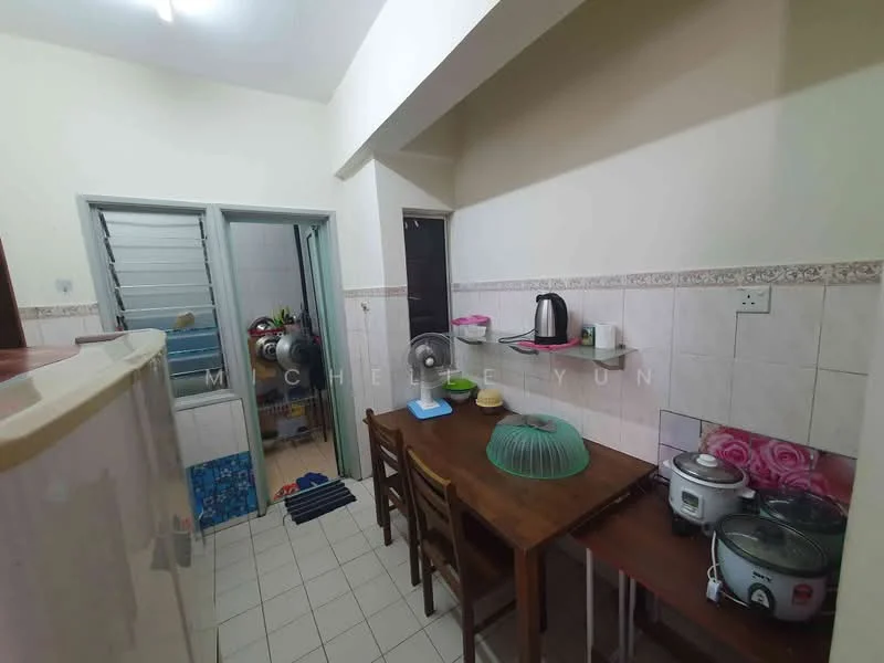 Kitchen features: white painted walls, cream tiled backsplash, ceramic tile flooring, wooden dining table with chairs, kettle, rice cooker, cooking pot, countertop with food cover, open shelving, refrigerator visible in adjacent room, window with metal grille, light fixture on ceiling.
