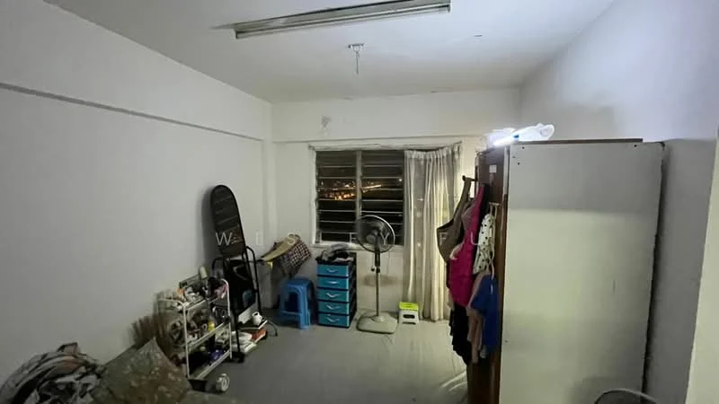 Room features: white painted walls, grey tiled flooring, window with sheer curtains, floor fan, wardrobe, shelving unit, blue storage drawers, clothes hanging on rack, decorative items on shelves; style: minimalist; view: city.