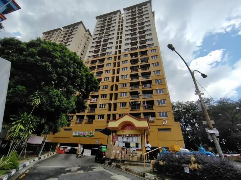 Exterior type: high-rise condominium; features: yellow painted facade, multiple storeys, balconies on upper floors, main entrance with awning, surrounded by greenery, street view with lamp posts, parking area visible in front, construction materials visible at base; style: modern.