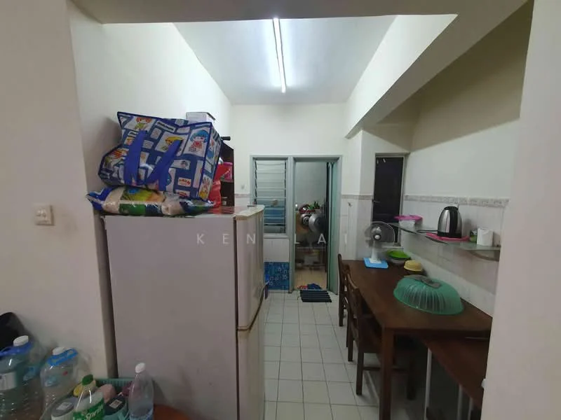 Kitchen features: white walls, tile flooring, refrigerator, wooden dining table, plastic dining chairs, kettle, sink, countertop, open shelving, stacked bags, water bottles, laundry area visible.