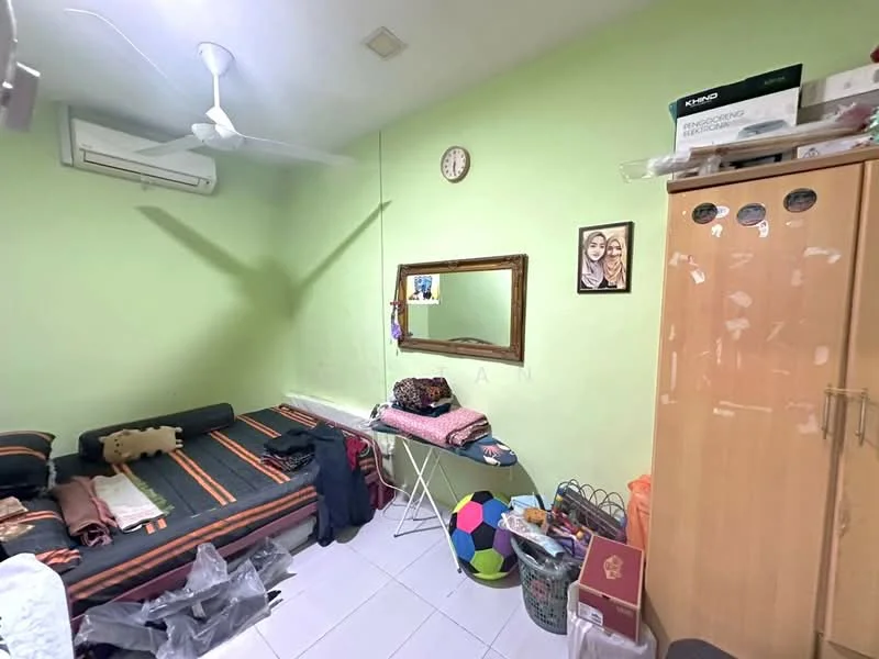 Bedroom features: green painted walls, white ceiling, 5-blade ceiling fan, wall-mounted air conditioning unit, wooden wardrobe, mirror on the wall, framed photographs, bed with patterned bedding, folding table, colorful soccer ball, various personal items on the floor.