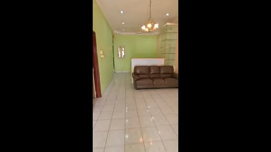 Living features: green painted walls, white tiled flooring, chandelier, 3-seater brown leather sofa, built-in shelving unit, mirror on wall, recessed lighting, open layout; style: modern.