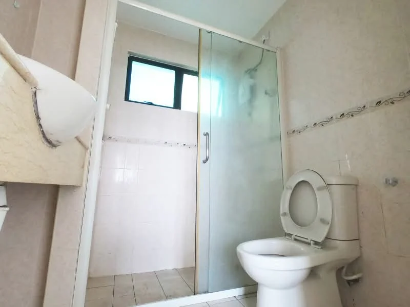 Bathroom features: white tiled walls, cream tiled flooring, glass shower enclosure, toilet, window, wall-mounted sink, decorative tile border.