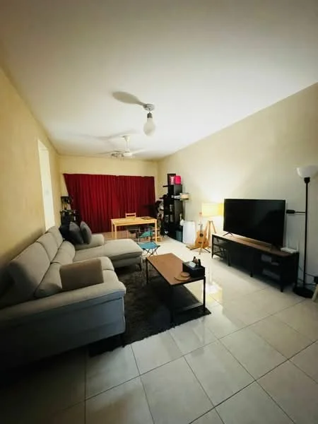 Living features: 3-seater fabric sofa in light grey, coffee table in dark wood, TV console in dark wood, wall-mounted TV, floor lamp, ceiling fan with light, area rug in dark colour, white painted walls, tiled flooring, red curtains, bookshelf with decorative items, dining table with chairs; style: modern.