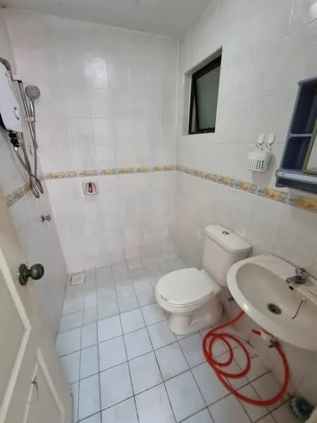 Bathroom features: white tiled walls, white tiled flooring, one-piece toilet, sink with chrome faucet, shower area with wall-mounted showerhead, window for natural light, towel rack, shower curtain rod, decorative border tile, exposed plumbing, red hose for water connection.