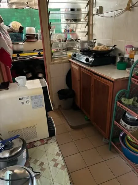 Kitchen features: wood cabinetry, white tiled walls, ceramic tile flooring, stainless-steel gas stove, kitchen countertop, sink, open shelving, trash bin, various kitchen utensils, stacked dishes, cooking pot, appliances including rice cooker, clothes drying rack.