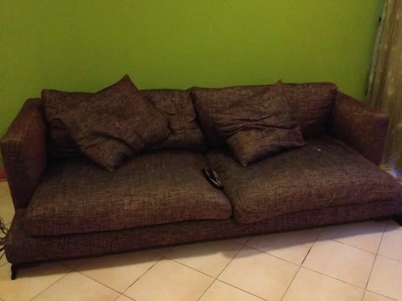 Living features: 3-seater fabric sofa in brown, decorative cushions, tile flooring, green painted walls, curtains, remote control on sofa.