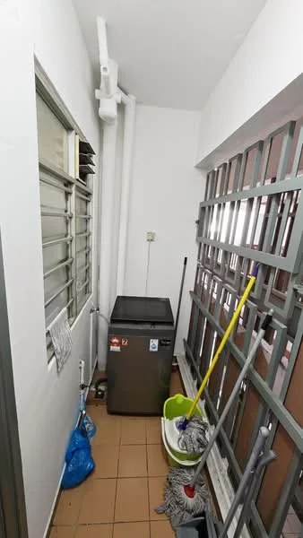Laundry features: grey chest freezer, white walls, brown tiled flooring, metal grilles on windows, cleaning mop, yellow broom, green bucket, blue plastic bag, white pipes along the wall.