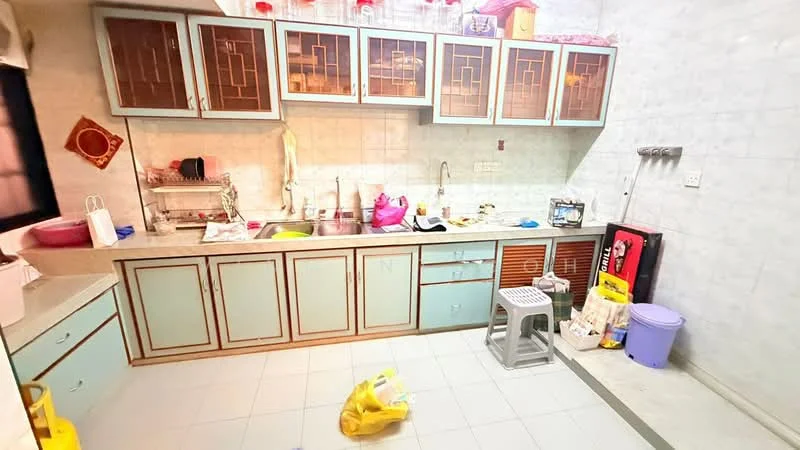 Kitchen features: light blue cabinetry with glass panels, white countertop, double-bowl stainless-steel sink, chrome faucet, wall-mounted storage shelves, tile backsplash, ceramic tile flooring, refrigerator, plastic stool, various kitchen items on countertop, plastic bags on floor, cleaning supplies.