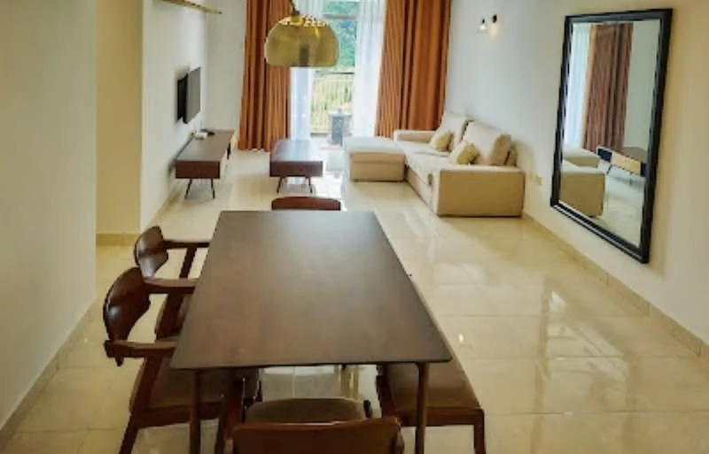 Living features: cream painted walls, glossy tile flooring, sofa in light beige fabric, wooden coffee table, wall-mounted TV, large mirror, floor-to-ceiling windows with sheer curtains, dining table with wooden surface, 4 wooden dining chairs, decorative wall sconces, curtains in orange, greenery view from window; style: modern; view: garden.