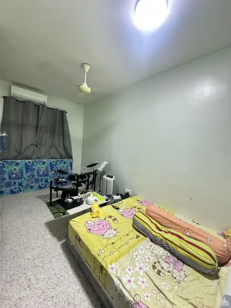 Bedroom features: single bed with patterned bedding, ceiling fan, wall-mounted air conditioning unit, grey curtains, light-colored painted walls, textured flooring, drum set, small table with items, decorative stuffed toy.