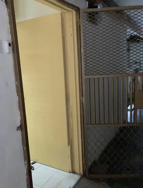 Room features: metal security gate, yellow painted door, white walls, tile flooring, exposed ceiling, dim lighting.