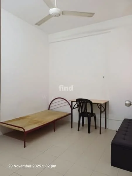 Room features: white painted walls, ceiling fan, tile flooring, single bed frame without mattress, wooden table, black plastic chair, black upholstered sofa, window with no visible treatment.
