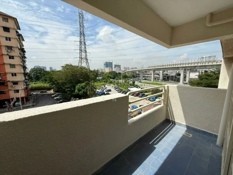 Balcony features: blue tiled flooring, railing with horizontal bars, view of city skyline, overlooking parking area, surrounded by greenery, electricity pylons visible, sunny weather, open space; view: city.