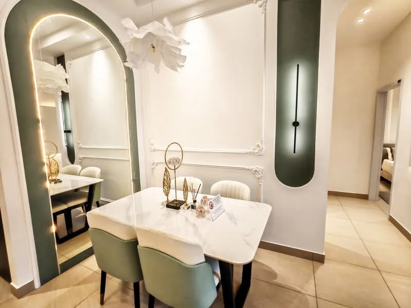 Dining features: marble dining table, 4 upholstered dining chairs in light green and cream, decorative wall paneling, mirror on wall, soft lighting fixture, neutral wall color, tile flooring, wall-mounted light fixture; style: modern.