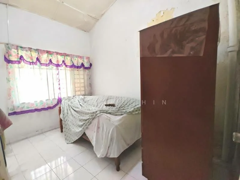 Bedroom features: single bed, white bedspread, wooden bed frame, curtains with floral pattern, white tiled flooring, wall with peeling paint, wardrobe with brown finish, window with natural light.