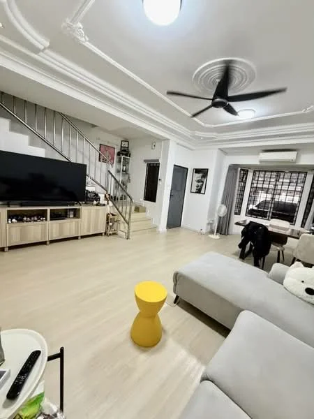 Living features: light wood flooring, white painted walls, crown moulding, 5-blade ceiling fan with light, wall-mounted TV, TV console with storage, sofa in light grey fabric, yellow accent table, large windows with security bars, air conditioning unit, staircase leading to upper floor, decorative wall art; style: modern.