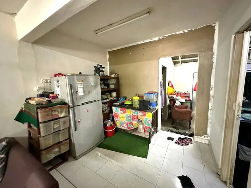 Kitchen features: white walls, tile flooring, stainless-steel fridge, wooden shelving unit, colorful tablecloth on table, green carpet, various kitchen utensils, open layout to adjacent room. Room features: white walls, tile flooring, dining table with chairs, decorative flags, open doorway to kitchen.