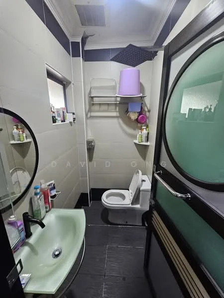 Bathroom features: green basin sink, chrome faucet, one-piece toilet, shower area with handheld shower, shelf for toiletries, mirror above sink, tile walls in light color, dark tile flooring, ventilation fan, glass shower door.