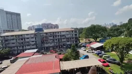 Exterior type: low-rise apartment block; features: multi-storey building, flat roof, red metal roofing, parking lot with multiple vehicles, manicured lawn, surrounding greenery, adjacent buildings in background, urban context with skyline view; style: modern.
