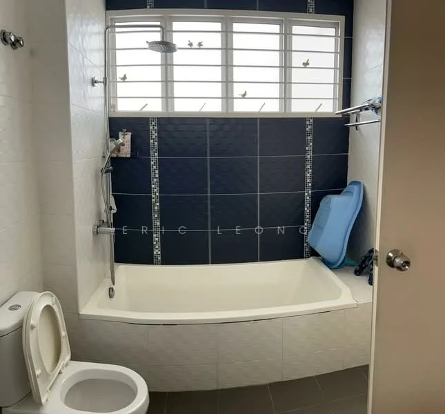 Bathroom features: bathtub, shower head, toilet, wall-mounted towel rack, blue bath mat, white tiled walls, dark blue accent wall, window with grid pattern, grey floor tiles.