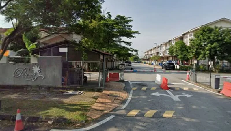 Exterior type: gated community; features: main entrance gate, guard house at entrance, paved driveway, landscaped greenery, traffic barriers, parking spaces, surrounded by trees, road markings, security signage; style: modern.