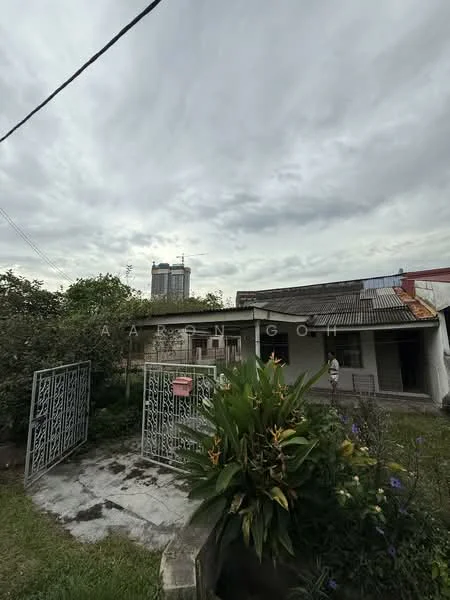Exterior type: detached bungalow; features: metal gate, concrete pathway, manicured lawn, garden with shrubs and flowers, single-storey structure, pitched roof, surrounded by greenery, adjacent to high-rise buildings; style: traditional.